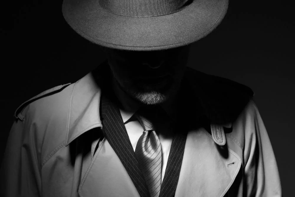 Mann posiert im Dunkeln mit Fedora-Hut und Trenchcoat